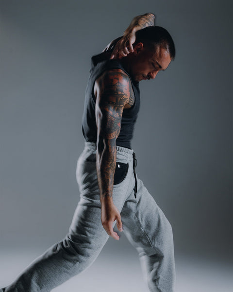 Man in black tank top and gray pants with tattoos on a gray background